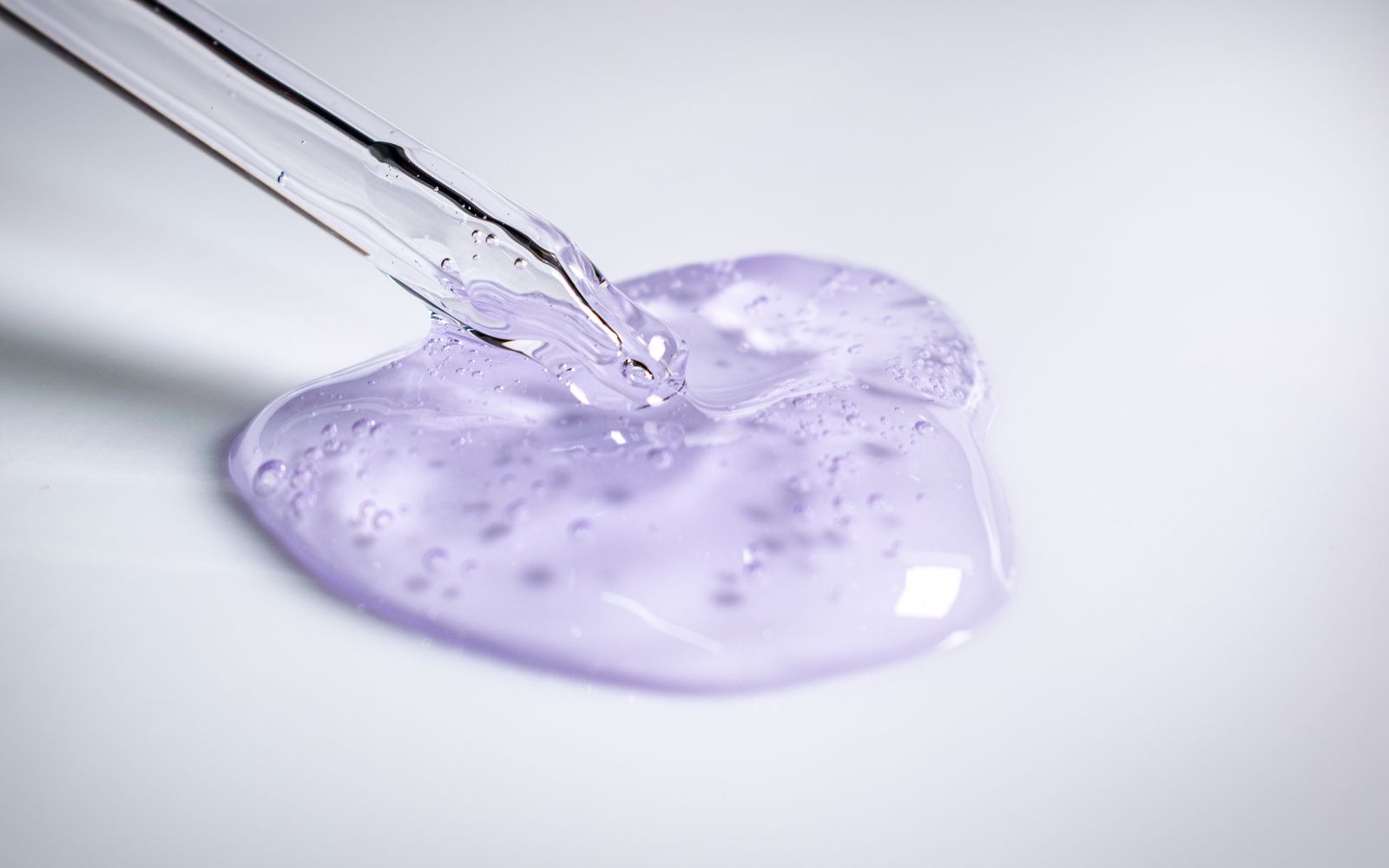 Una goccia di gel trasparente che cade da una pipetta di vetro su una superficie chiara