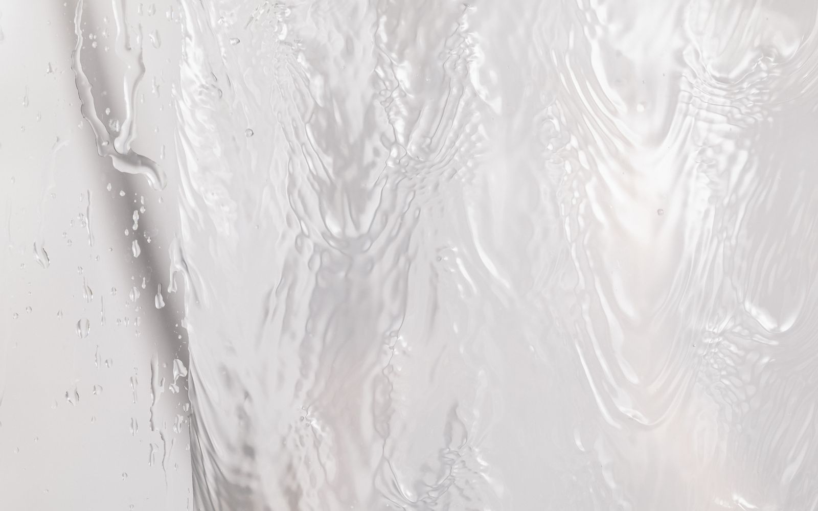 Acqua che scorre in modo morbido su una superficie chiara, con riflessi di luce e piccole gocce