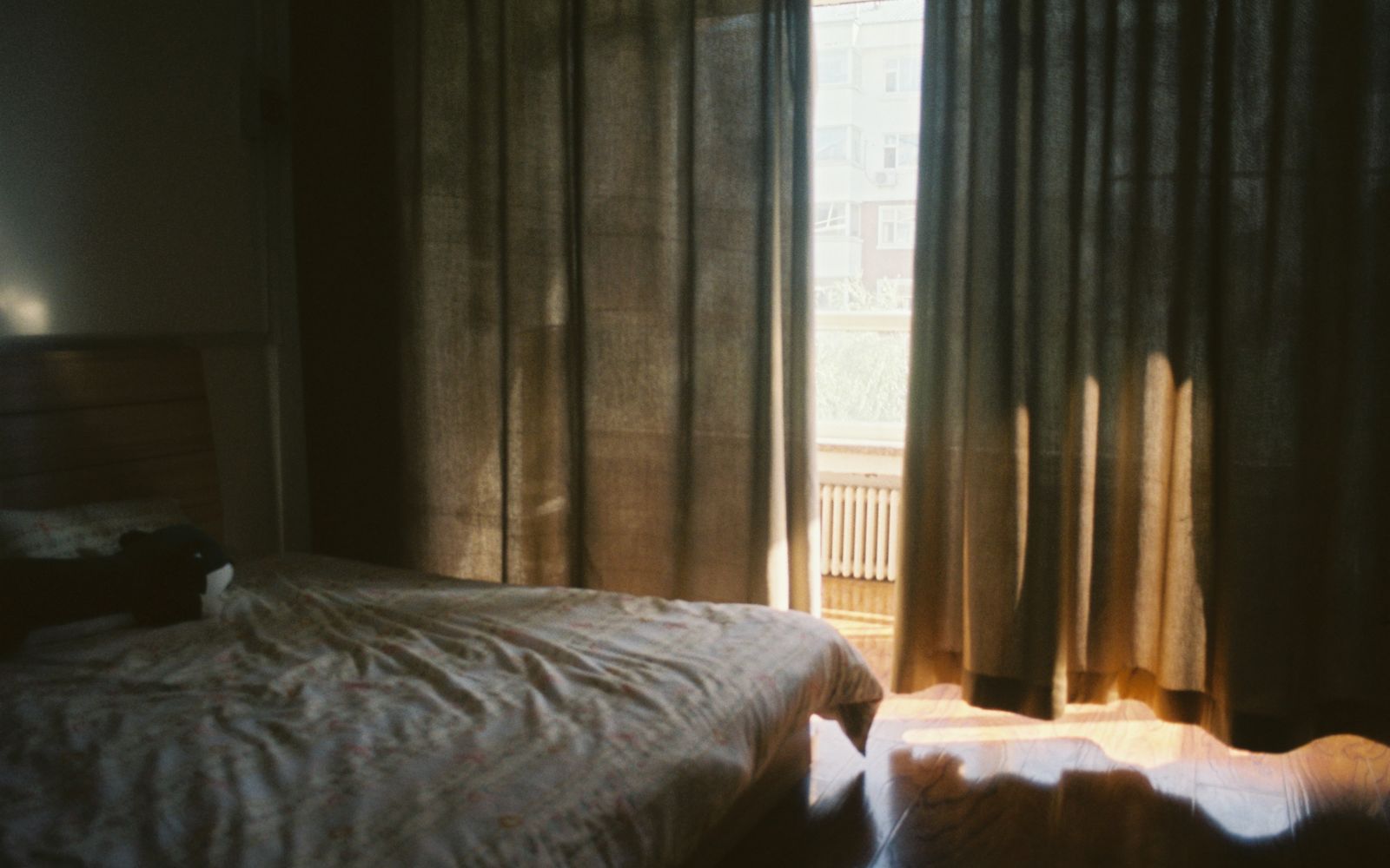 Camera da letto con le tende illuminate dal sole del mattino e un letto con le lenzuola spiegazzate