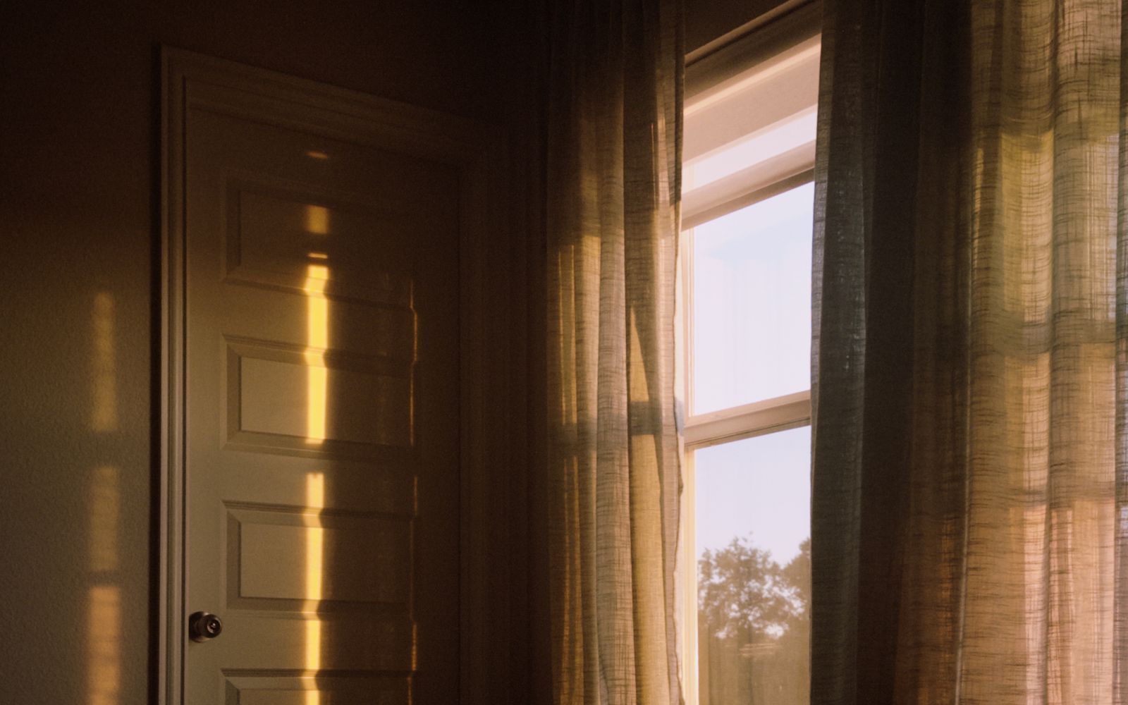 Luce dorata del tramonto su una porta chiara e su una tenda leggera, in una stanza raccolta